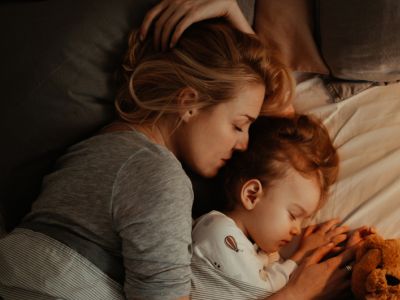 A mom and daughter cuddling in bed; positive parenting can help kids overcome sleep problems.