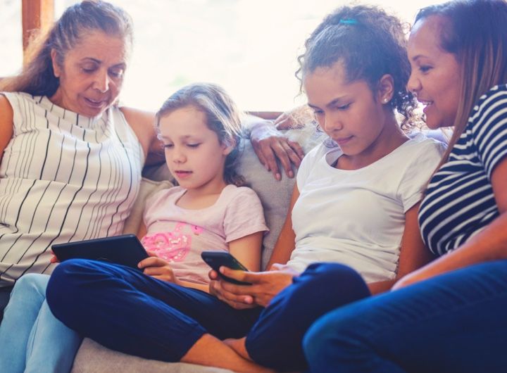 family sitting on couch talking - two children are looking at devices