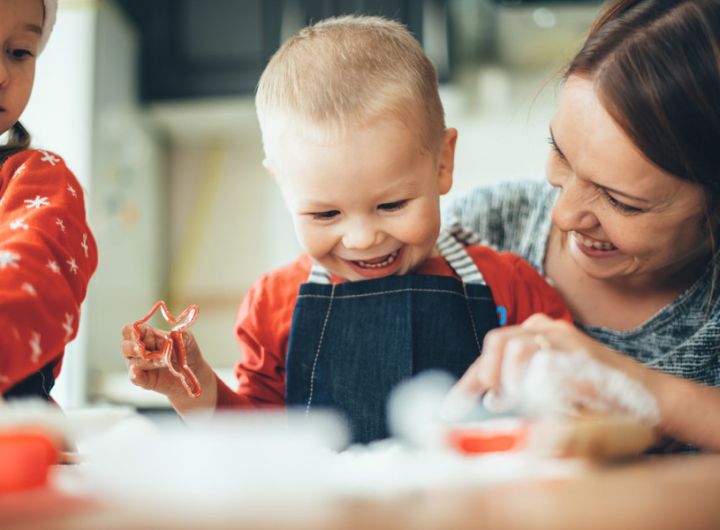 happy baby cuts pastry dough as mother and sibling look on