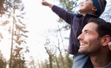 boy riding on dad's shoulders points excitedly to the sky