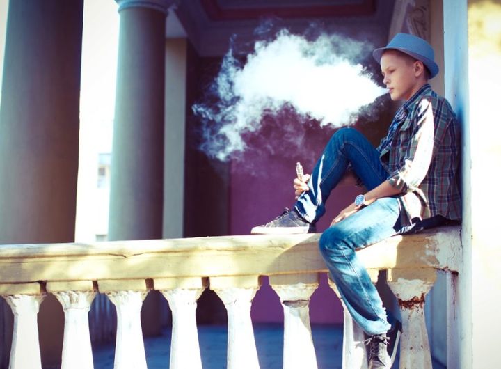 teenage boy blowing smoke from vaping device