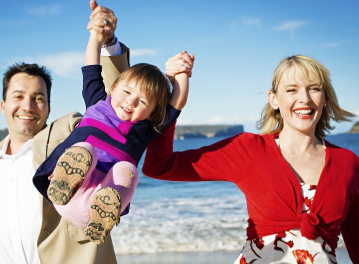 母親と父親が幼児を高く持ち上げている、海岸で遊ぶ幸せな家族